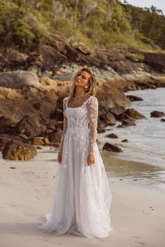 a woman standing on top of a beach next to the ocean wearing a wedding dress