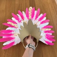 a person is holding a pink and white feathered headdress on a wooden table