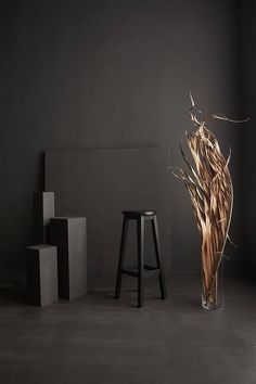 a tall glass vase sitting next to two stools on top of a cement floor