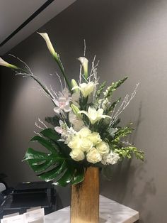 a vase filled with white flowers and greenery on a marble counter top next to a gray wall