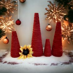 three red cone trees with a sunflower in the center and christmas decorations behind them