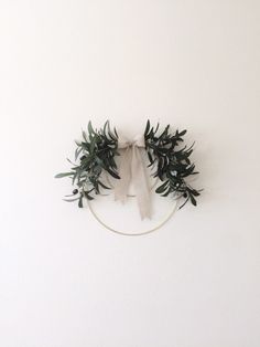 an olive wreath hanging on the wall with a white ribbon around it and some green leaves