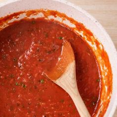 a wooden spoon in a white bowl filled with marinara sauce on a wood table