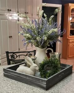 a white vase filled with purple flowers on top of a kitchen counter next to a bunny figurine