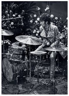 a man sitting on top of a drum set in front of a bunch of flowers