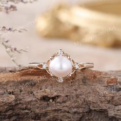 a white pearl and diamond ring sitting on top of a piece of wood with flowers in the background