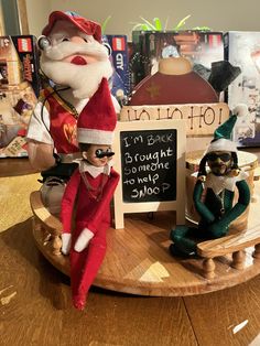 two elf figurines sitting on top of a wooden table next to a sign