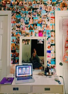 a laptop computer sitting on top of a desk in front of a wall covered with pictures