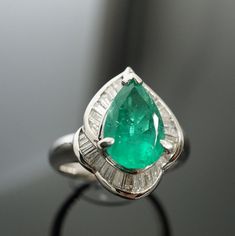 "Colombian Pear Shaped 1.86ct Emerald Ring D:0.62ct Emeralds are mined in many countries; however, Colombian emeralds are often the most prized as they have a very pure colour and are reputed as being one of the most natural gemstones. It is also regarded as May Birthstone in western astrology. A lovely platinum made ring featuring a 1.86 carat pear-shape Colombian emerald. It has a bright gem green color with excellent brilliance and life. It Is accented by 0.62 carats of baguette diamonds set Gia Certified Green Pear-shaped Diamond Ring, Gia Certified Pear-shaped Diamond Emerald Ring, Gia Certified Pear-shaped Emerald Ring, Green Wedding Rings, Western Astrology, Promise Rings Vintage, Smaragd Ring, Emerald Ring Gold, Gold Promise Rings