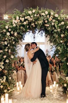 a bride and groom kissing in front of an arch of flowers at their wedding ceremony