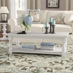 a living room with white furniture and blue flowers on the coffee table in front of it