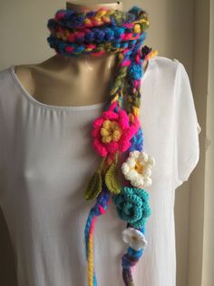 a woman wearing a white shirt and multicolored crocheted scarf on top of a mannequin