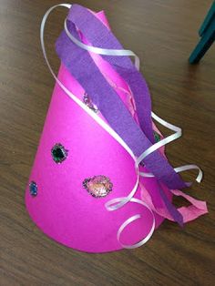 a pink hat with purple ribbon and sequins on it sitting on a wooden table