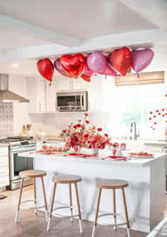 some balloons are hanging from the ceiling above a kitchen island with stools and table