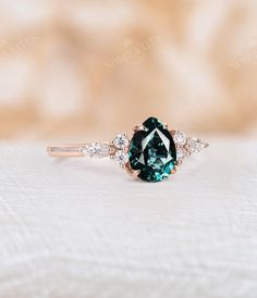 an oval cut green and white diamond ring on top of a bed with a beige background