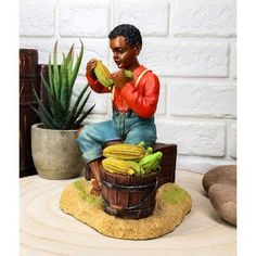 a figurine of a man eating corn on the cob next to a potted plant