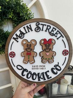 a person holding up a sign that says main street cookie co with two teddy bears on it