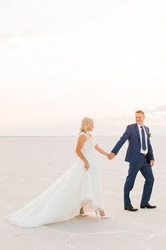 a bride and groom holding hands while walking across an ice covered field with the sun setting in the background