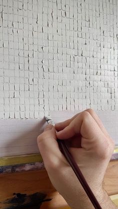 a person holding a pencil in their left hand while painting a wall with white paint