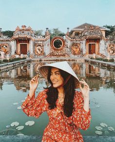 a woman standing in front of a pond wearing a hat