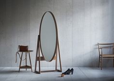 an oval mirror sitting next to a wooden chair and table with high heel shoes on the floor