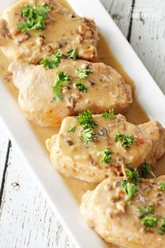 three pieces of chicken covered in gravy on a white plate with parsley