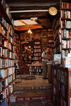 a man standing in the doorway of a book store filled with lots of books on shelves