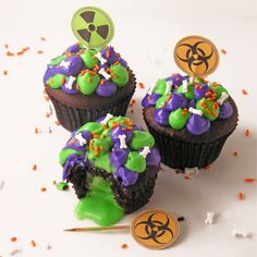 two cupcakes with green and purple frosting on them, one has a biohazard top