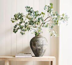 a vase filled with green leaves on top of a wooden table