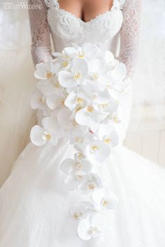 a woman in a white wedding dress holding a bouquet of orchids on her back