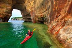 a man in a kayak is paddling through the water near a rock formation