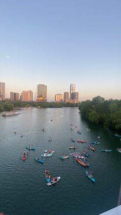 many people are in canoes on the river with tall buildings behind them and skyscrapers