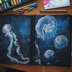 an art journal with jellyfishs and space in the background, surrounded by colored crayons