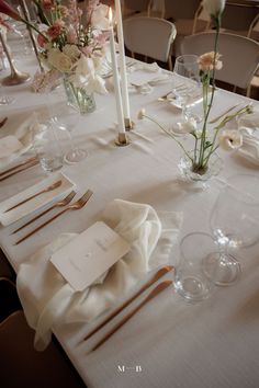 the table is set with white linens and silverware, candles, and flowers