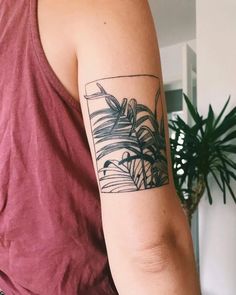 a woman with a tattoo on her arm is standing in front of a potted plant