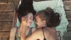 two young women laying next to each other on top of a bed