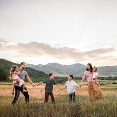 a family is holding hands and walking through the grass with mountains in the background at sunset