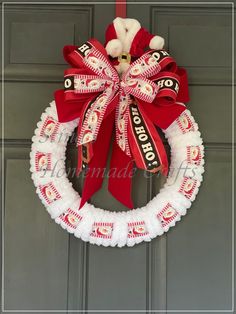 a red and white christmas wreath hanging on a door with a teddy bear wearing a santa hat