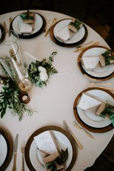 the table is set with white and gold plates, silverware, greenery and napkins