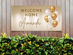 a welcome sign with gold and white balloons hanging from it's side on a wooden wall