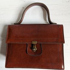 A lovely vintage brown handbag with a carry handle and in a traditional boxy shape The handbag is made from brown faux leather. There in one large internal compartments with a smaller zip pocket on the inside. The handbag fastens with a metal clasp which is still very strong The handbag measures approx 22.5cm x 19cm x 6cm. The strap is 24cm long. The bag is in really good condition Ideal bag to complete a vintage outfit Brown Rectangular Shoulder Bag With Top Carry Handle, Brown Rectangular Box Bag With Carry Handle, Brown Office Satchel, Brown Box Bag With Handle Drop Top Handle, Brown Box Bag With Handle Drop And Top Handle, Brown Top Handle Box Bag With Handle Drop, Formal Cognac Satchel With Handles, Brown Tote Box Bag With Detachable Handle, Brown Rectangular Box Bag