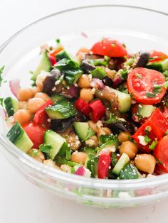 a salad in a glass bowl with tomatoes, cucumbers and chickpeas