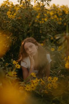 a woman sitting in the middle of a field of yellow flowers with her hand on her face