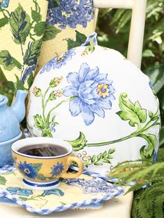 a blue tea pot sitting on top of a white chair next to a cup and saucer