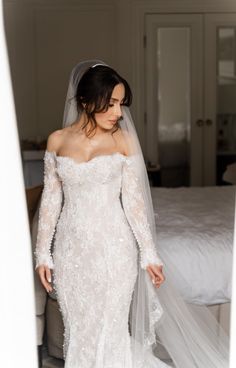 a woman wearing a wedding dress and veil standing in front of a bed with white sheets