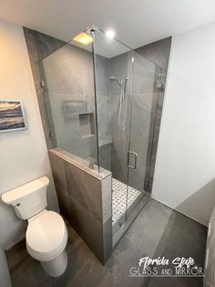 a bathroom with a walk in shower next to a white toilet and gray tiled walls