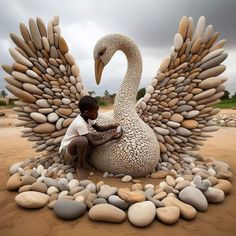 a boy sitting on top of a large bird made out of rocks and pebbles in the sand