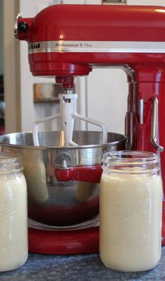 a red mixer sitting on top of a counter next to two jars filled with milk