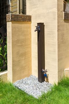 a water spigot in front of a building with grass and rocks on the ground