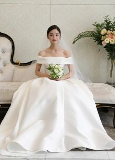 a woman in a white wedding dress sitting on a couch next to a flower arrangement